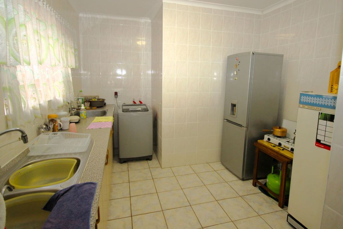 A functional kitchen featuring tiled walls and floors, a double sink, and dedicated space for laundry appliances.