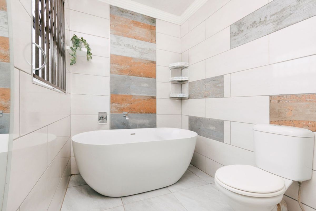A modern bathroom featuring a freestanding bathtub, a wall-mounted toilet, and decorative accent tiling on the walls.