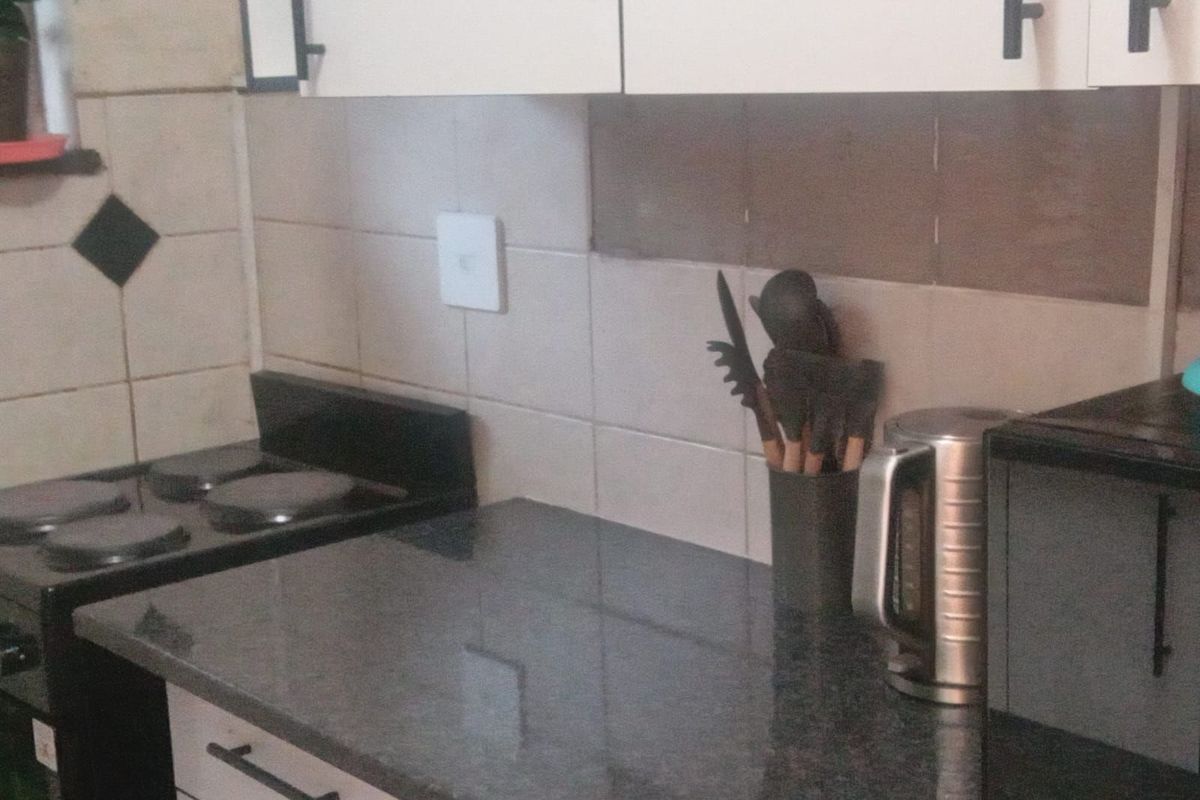A compact kitchen area featuring dark stone countertops, white cabinetry, and a built-in electric stove with tiled splashback.