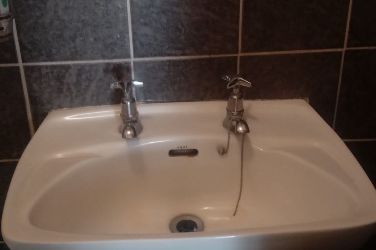 A close-up view of a bathroom vanity basin featuring traditional chrome taps and dark tiled splashback.