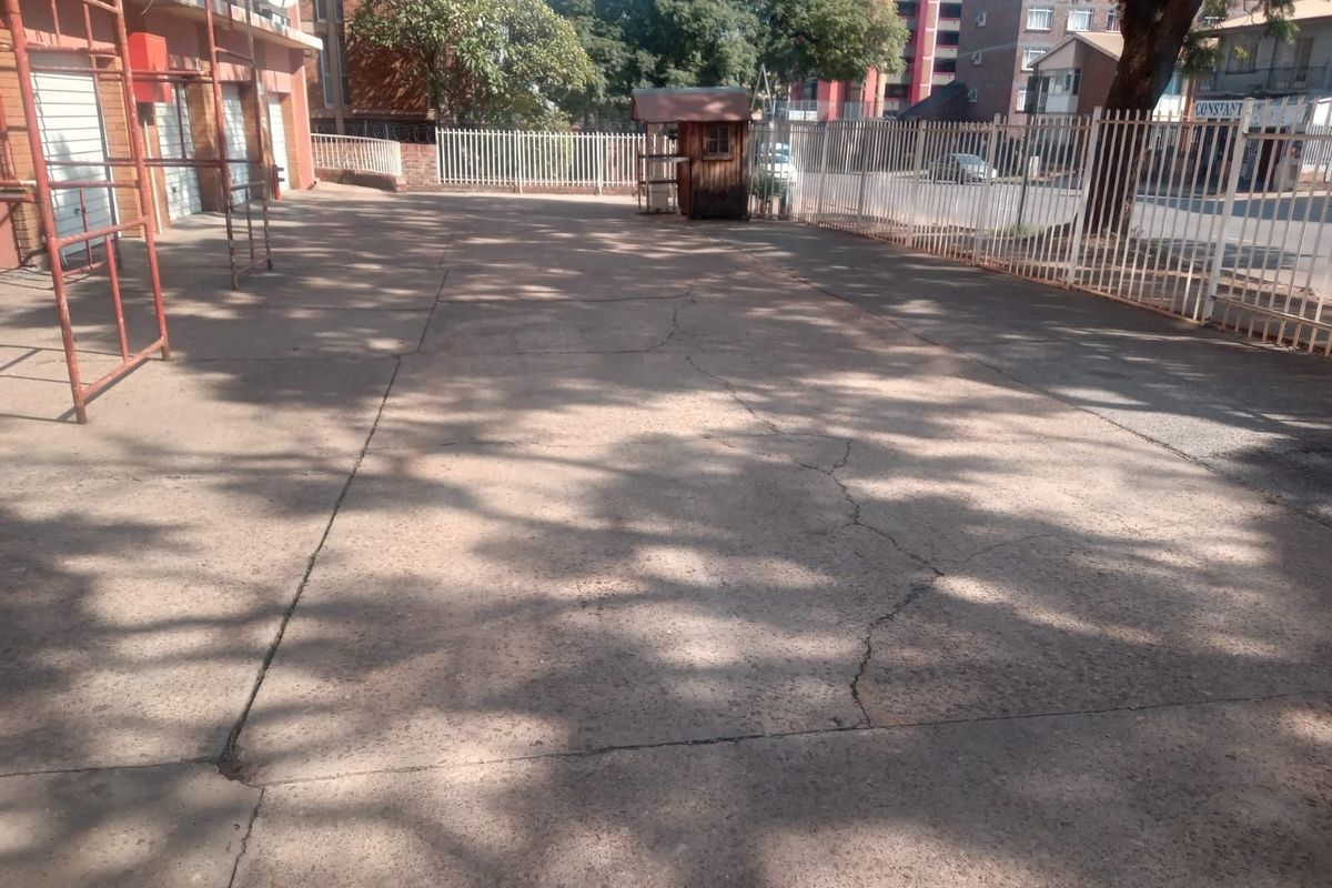 An exterior view of a paved parking or driveway area featuring perimeter metal fencing and a small guard hut structure.