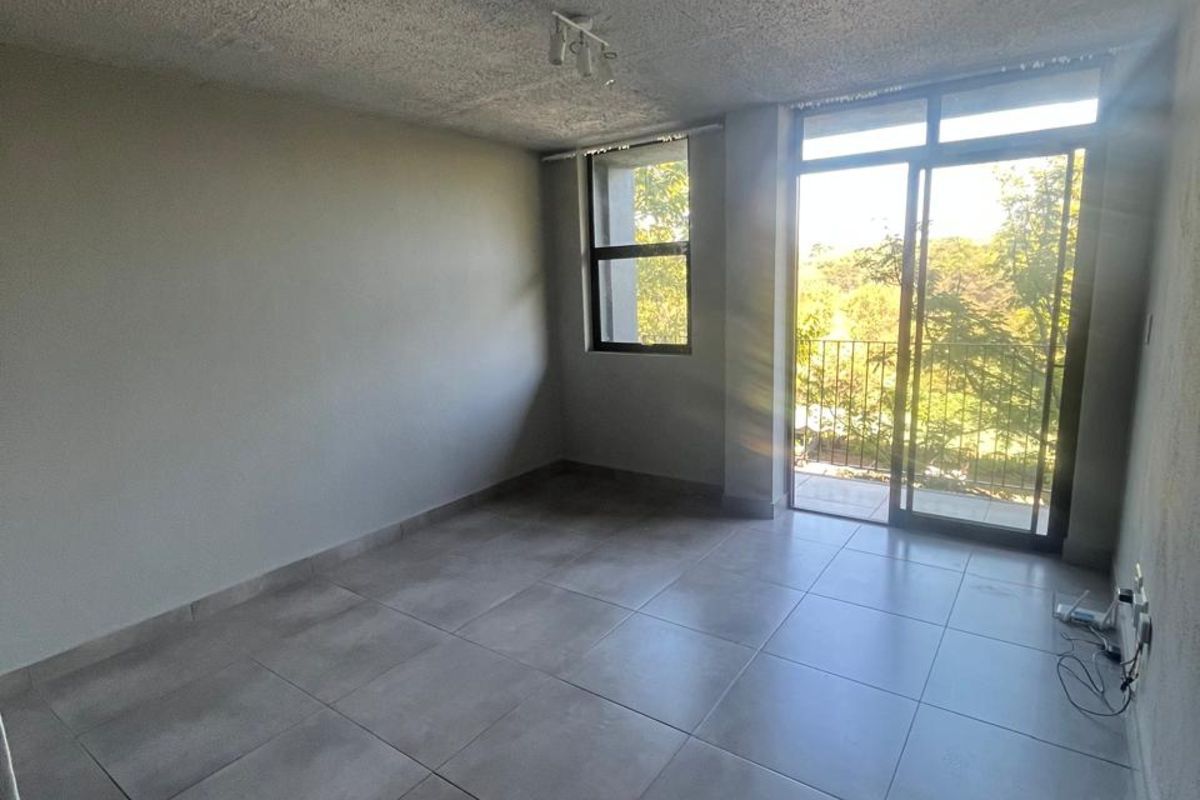 An empty living room featuring large format floor tiles, a textured ceiling, and sliding glass doors leading to a balcony with natural light.