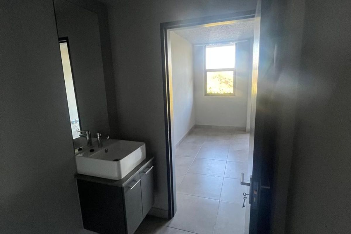 A compact bathroom featuring a wall-mounted vanity with a vessel sink, leading into an adjacent room with tiled flooring and natural light.