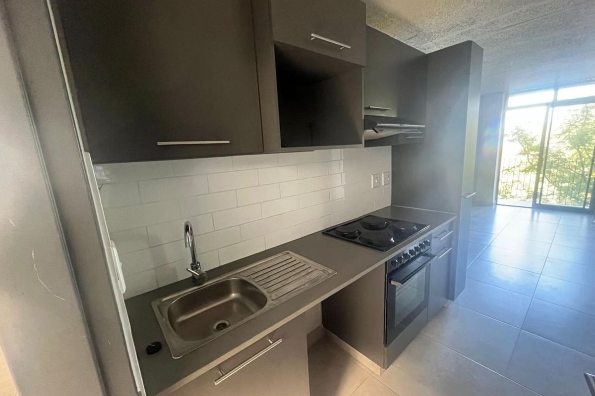 Modern galley-style kitchen featuring dark cabinetry, a built-in oven, electric hob, extractor fan, and a stainless steel sink with subway tile backsplash.