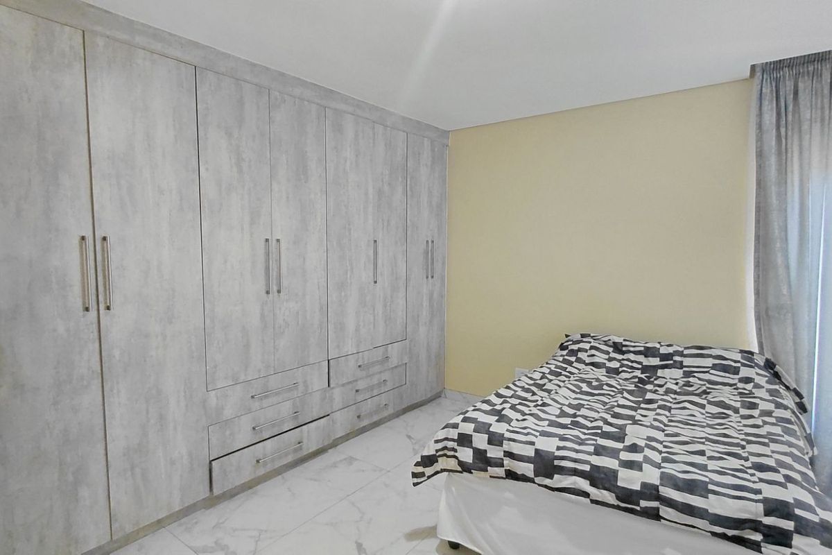 A well-maintained bedroom featuring extensive built-in cabinetry with a modern grey wood-grain finish and polished marble-look floor tiles.