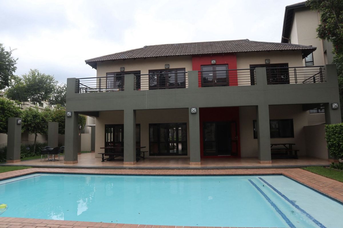 Rear view of a two-story apartment building featuring a covered patio, upper balcony with metal railings, and a private swimming pool.