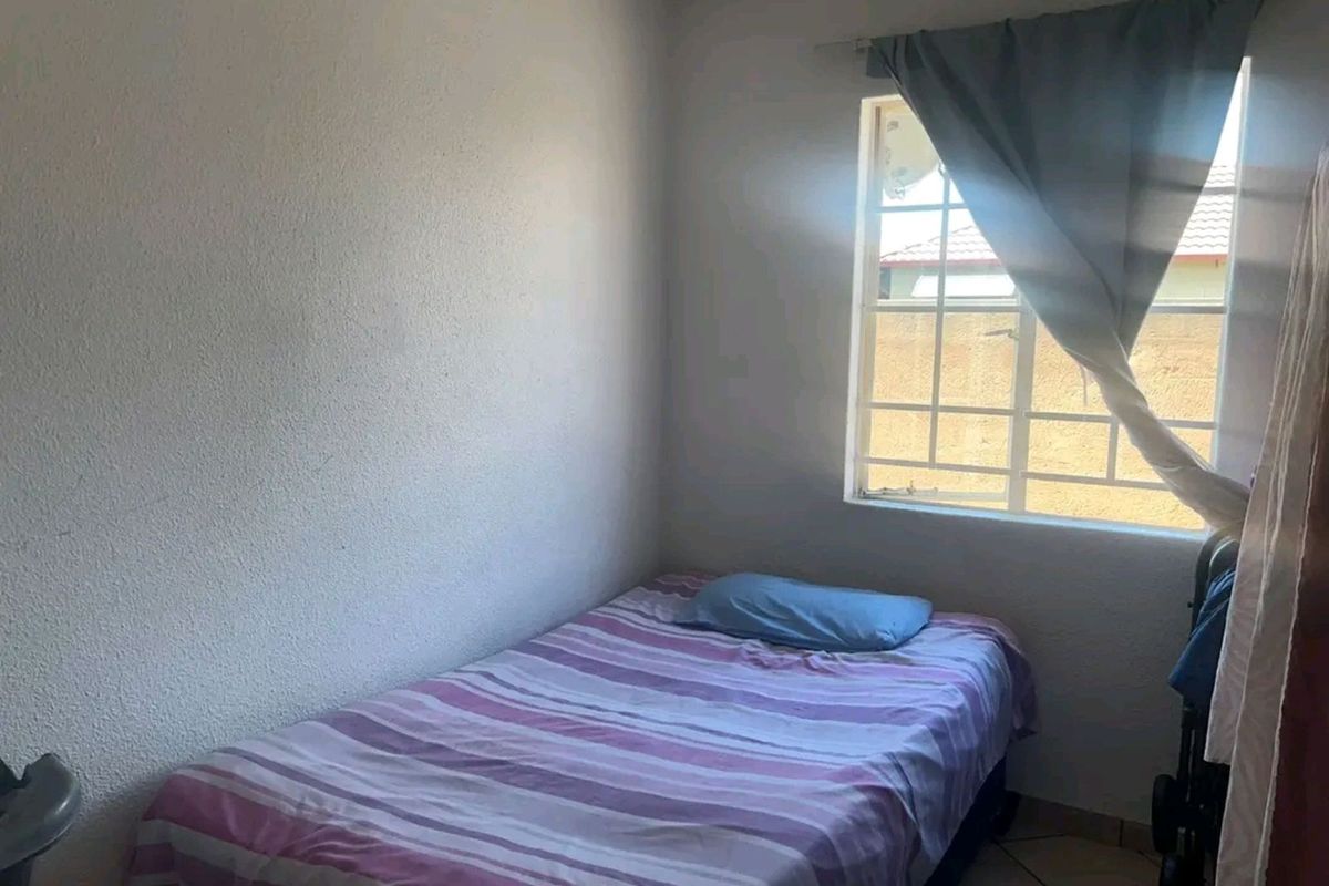 A compact bedroom featuring tiled flooring and a window with security bars, providing natural light.