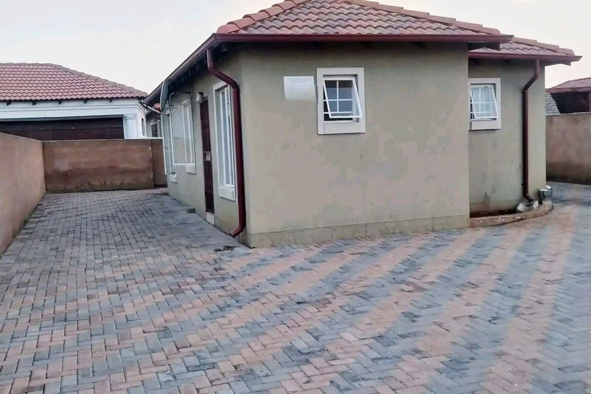 A view of the rear exterior of the house featuring a paved courtyard area, tiled roof, and perimeter boundary walls.