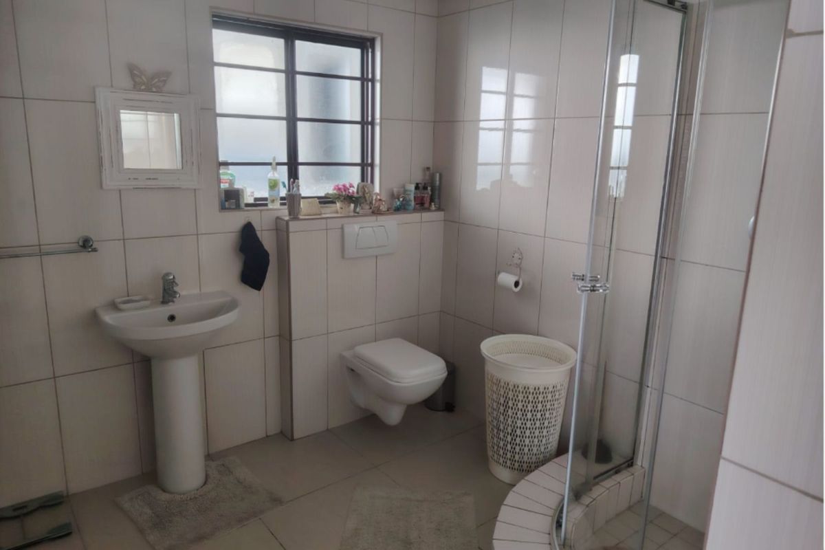 A functional bathroom featuring a pedestal basin, wall-mounted toilet, and a corner shower enclosure with glass doors and tiled surround.