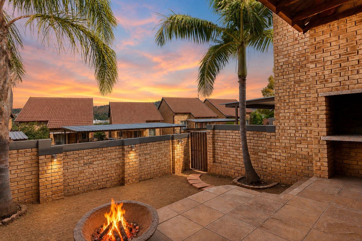A private rear courtyard featuring a paved patio, built-in brick braai, and a fire pit area, enclosed by a brick boundary wall.