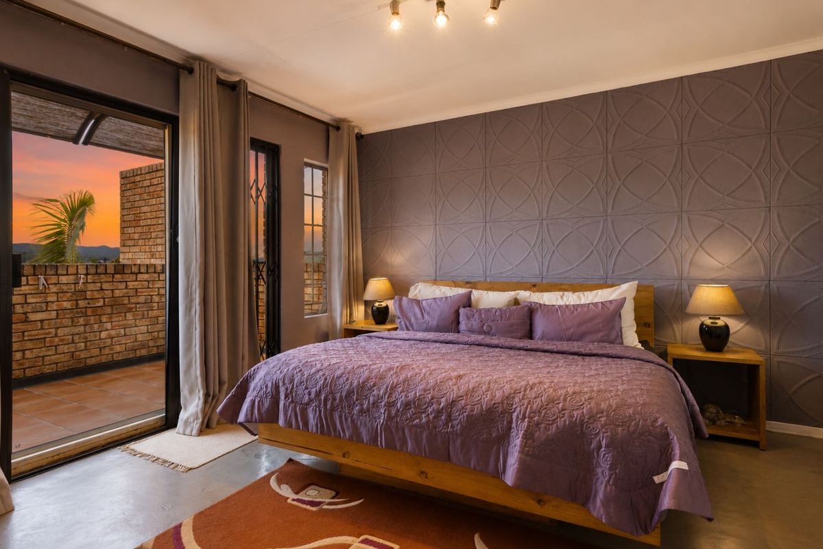 Spacious bedroom featuring a textured feature wall, polished concrete flooring, and direct access to a private balcony with sunset views.