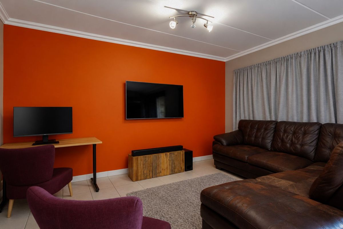 A living room featuring tiled flooring, a prominent orange accent wall, and ceiling-mounted lighting fixtures.
