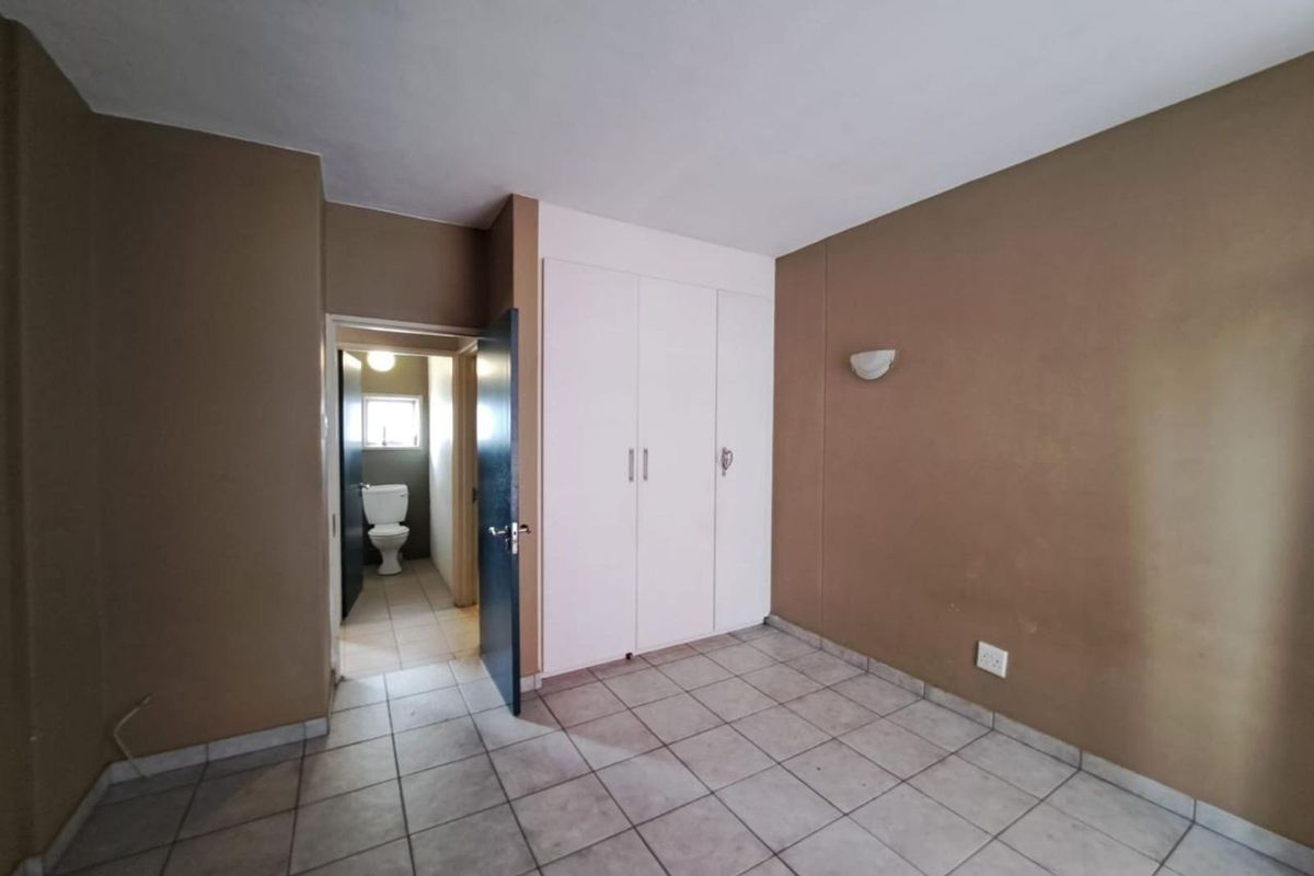 A bedroom featuring built-in cupboards and tiled flooring, with an adjoining en-suite bathroom visible through the doorway.