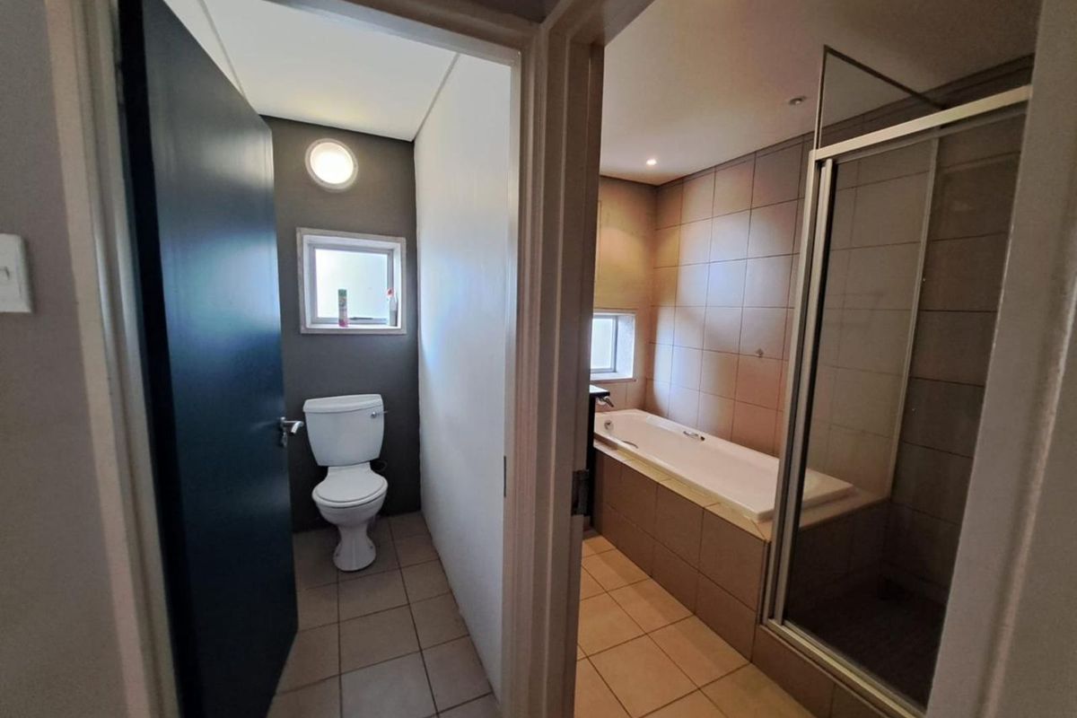 A functional bathroom featuring a separate toilet area, a built-in bathtub, and a glass-enclosed shower with neutral floor and wall tiling.