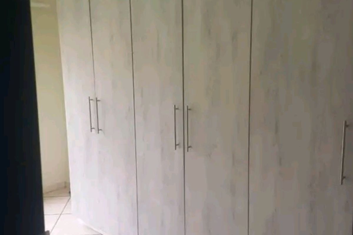 A bedroom featuring floor-to-ceiling built-in cupboards with a light wood-grain finish and tiled flooring.