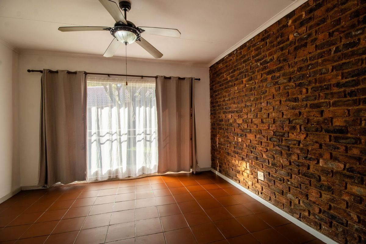A bright bedroom featuring a rustic exposed brick feature wall, tiled flooring, and a ceiling fan, with sliding door access to the exterior.