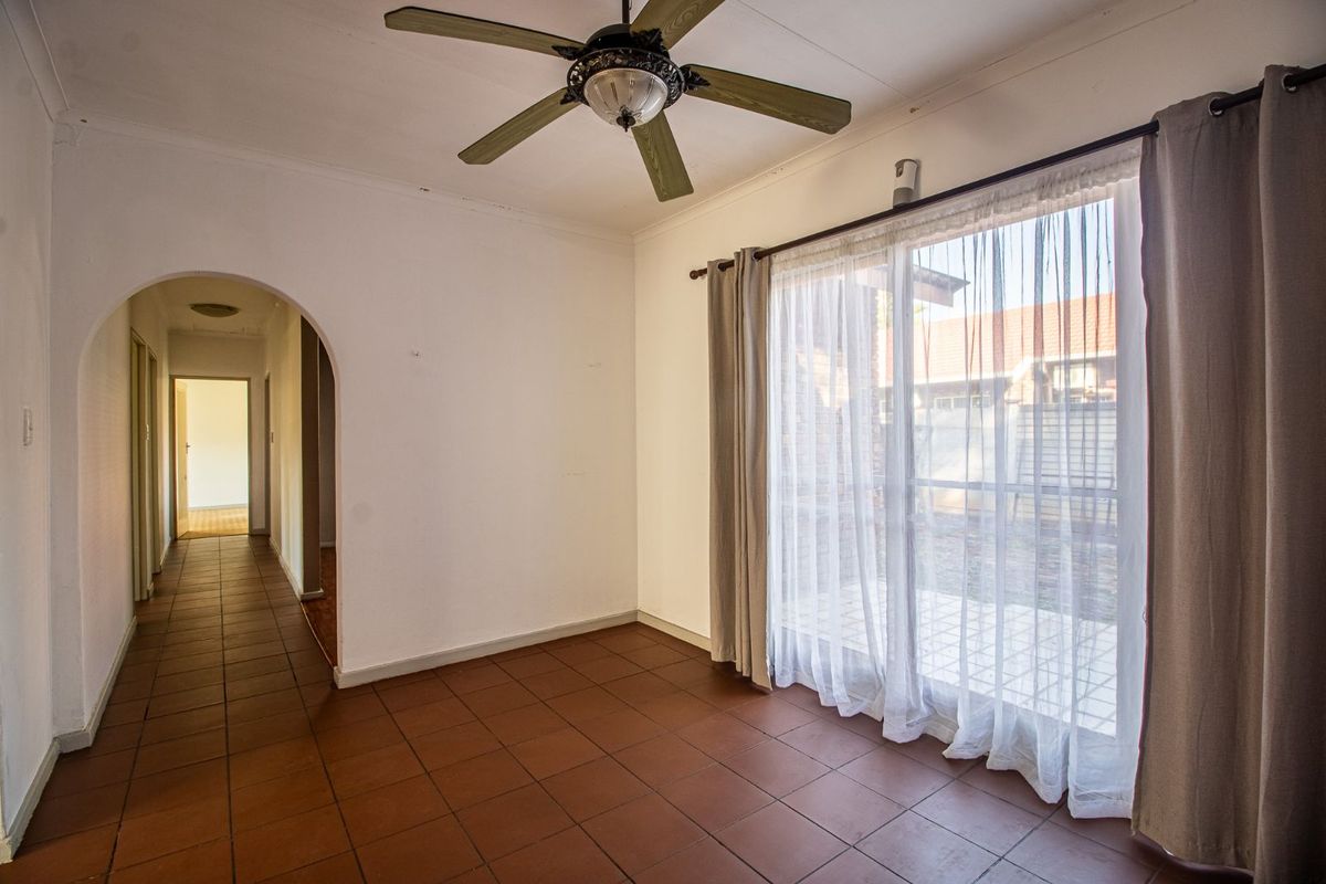 A bright, empty living room featuring terracotta floor tiles, a ceiling fan, and large sliding glass doors providing access to the exterior.