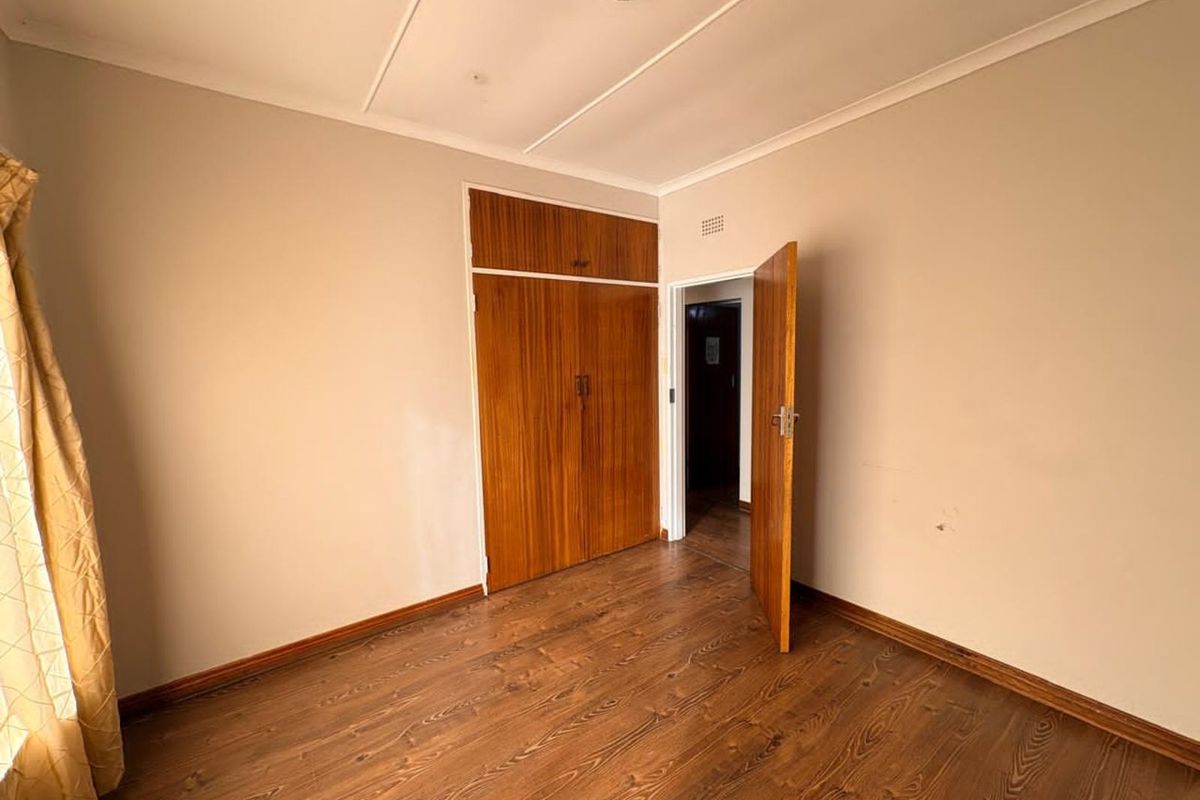 A bedroom featuring wood-look laminate flooring, built-in wooden cupboards with overhead storage, and a standard interior door.