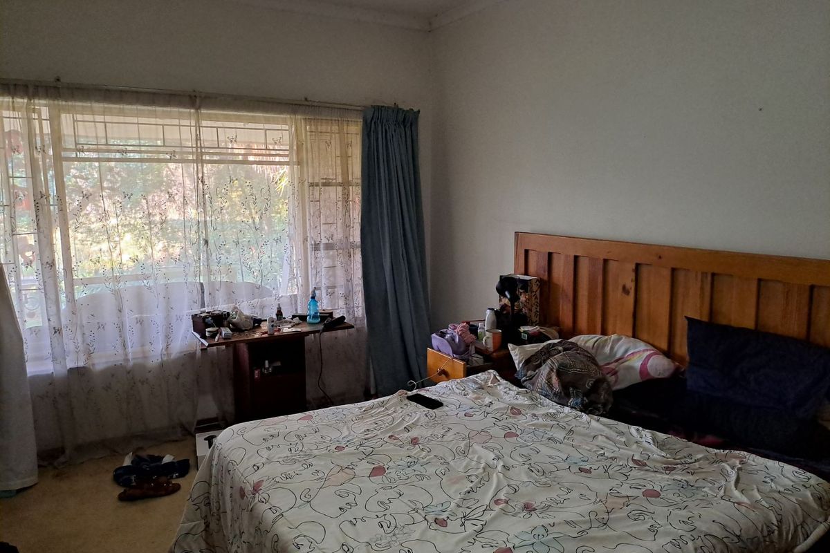 A bedroom featuring a large window with natural light, carpeted flooring, and a wooden headboard.