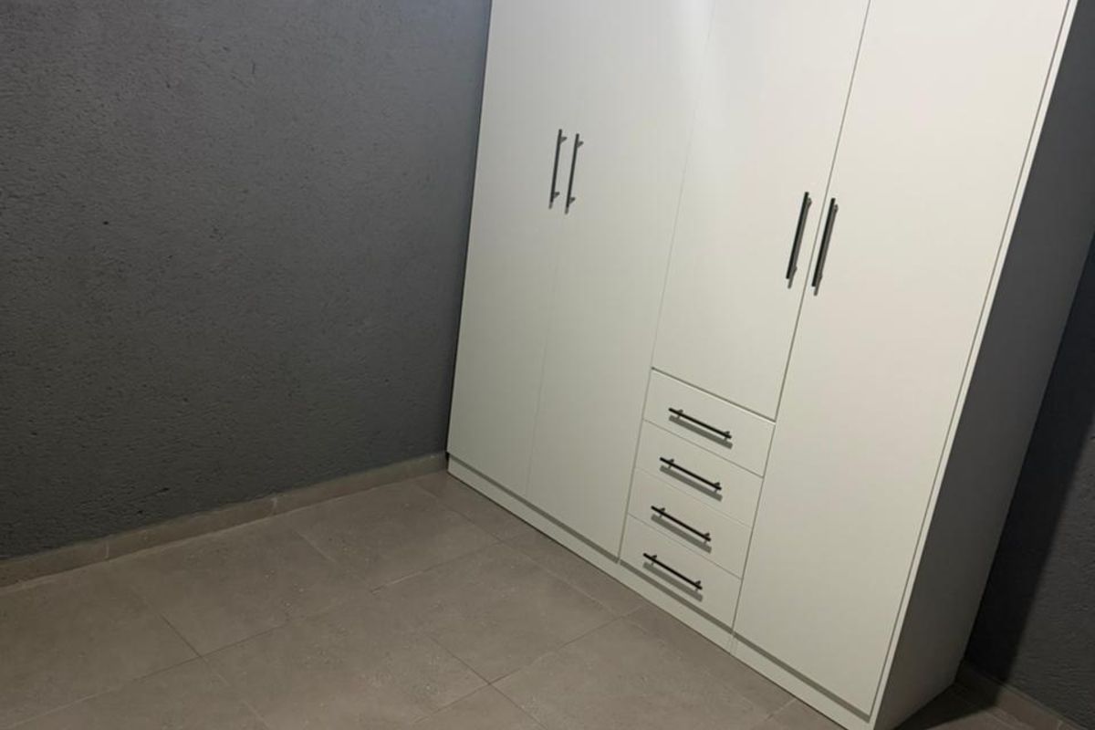 A bedroom featuring neutral floor tiles, dark grey textured walls, and a large, white built-in wardrobe with integrated drawers.