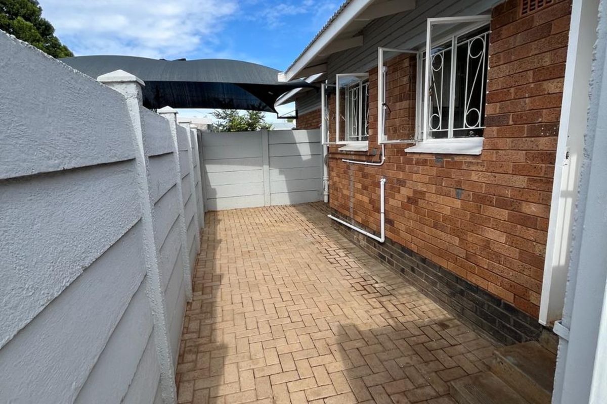 A side exterior walkway featuring brick paving, a face-brick wall finish, and secure metal window burglar bars.