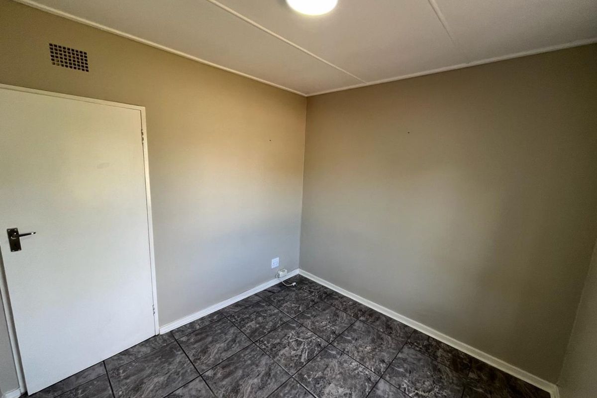 A clean, empty bedroom featuring neutral wall tones and dark marble-effect floor tiles, providing a versatile space ready for personalization.