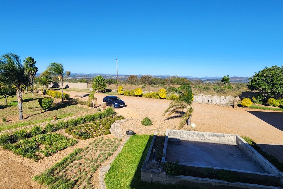 An elevated view of the property grounds featuring a large unpaved driveway, landscaped garden beds, and an unfinished concrete outdoor structure.