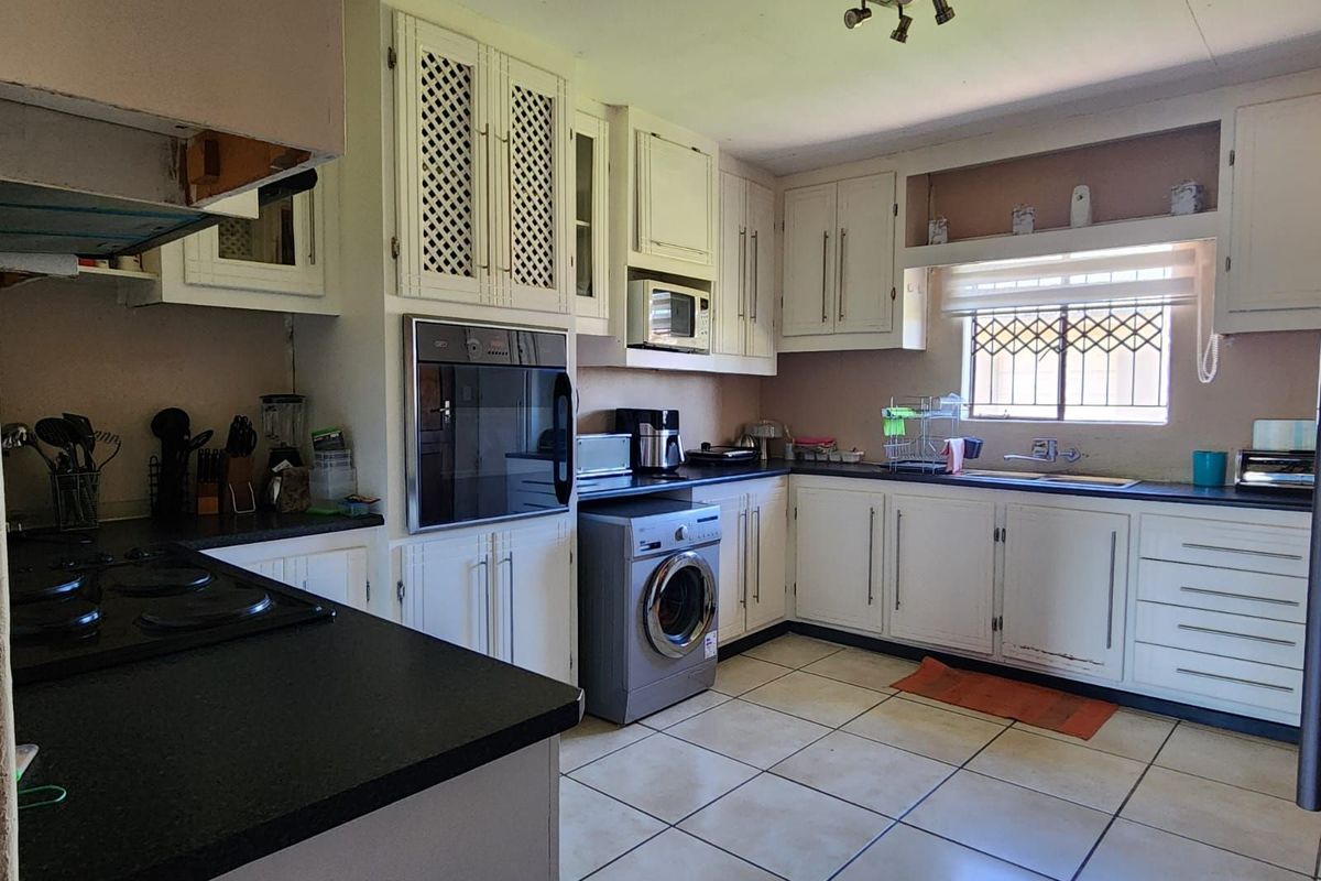 A functional kitchen featuring white cabinetry, dark countertops, built-in oven, and integrated laundry space with tiled flooring and natural light.