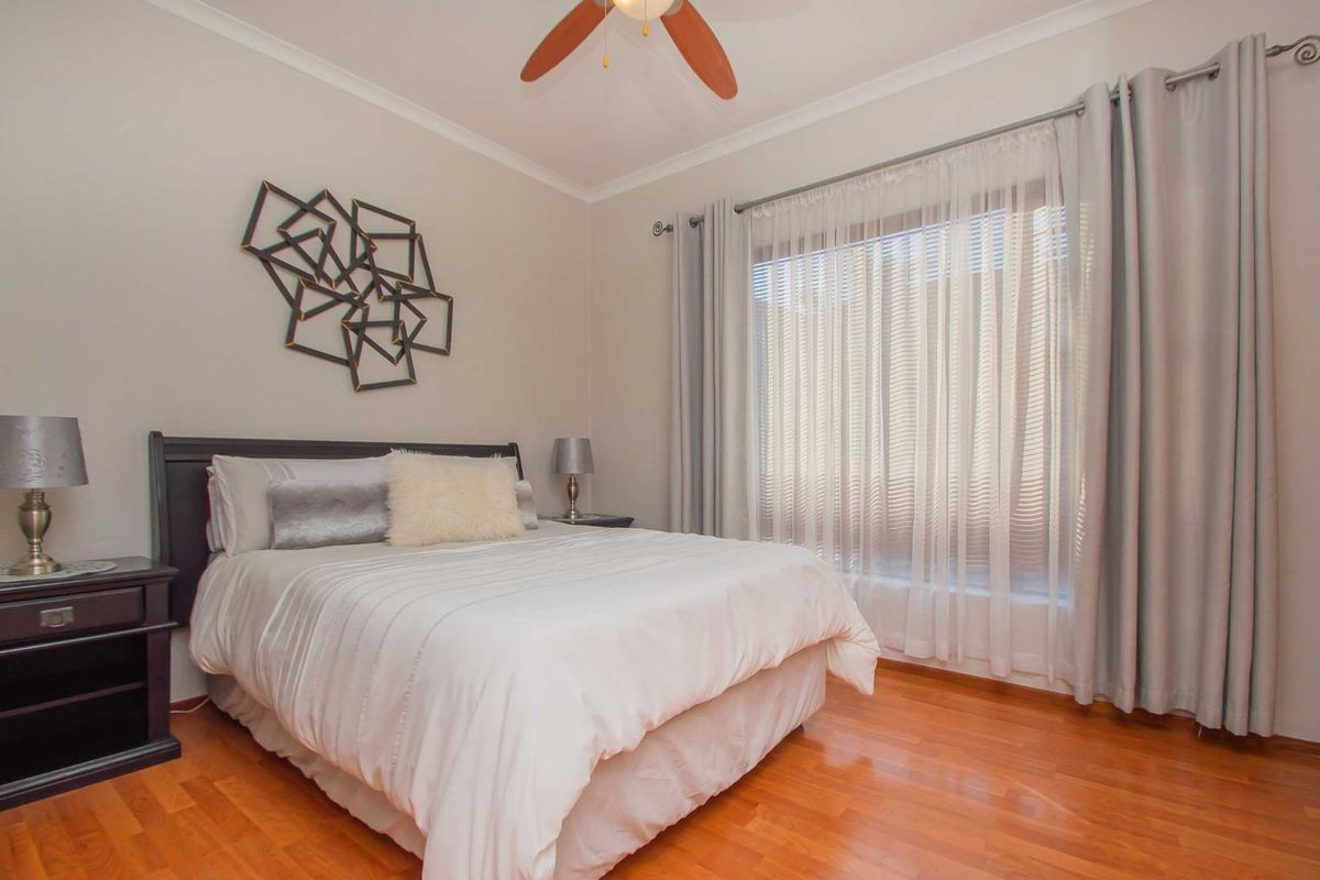 A well-maintained bedroom featuring warm-toned laminate flooring, a ceiling fan, and large windows with curtain tracks.