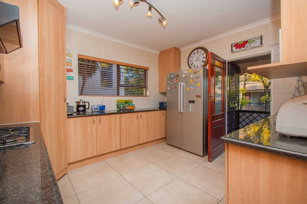 A functional kitchen featuring light wood-finish cabinetry, dark granite countertops, tiled flooring, and a built-in gas hob with an extractor fan.