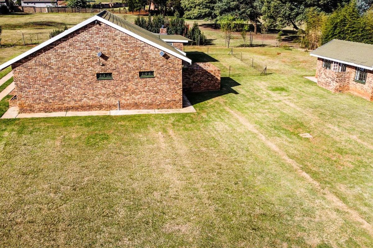 Aerial view of the property showing the main brick house and a separate outbuilding set within a large, expansive garden area.