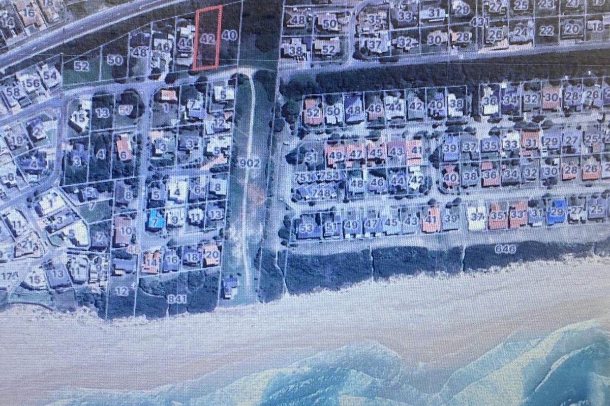 Aerial view of a residential vacant land plot highlighted in red, situated within a coastal neighborhood near the beach.
