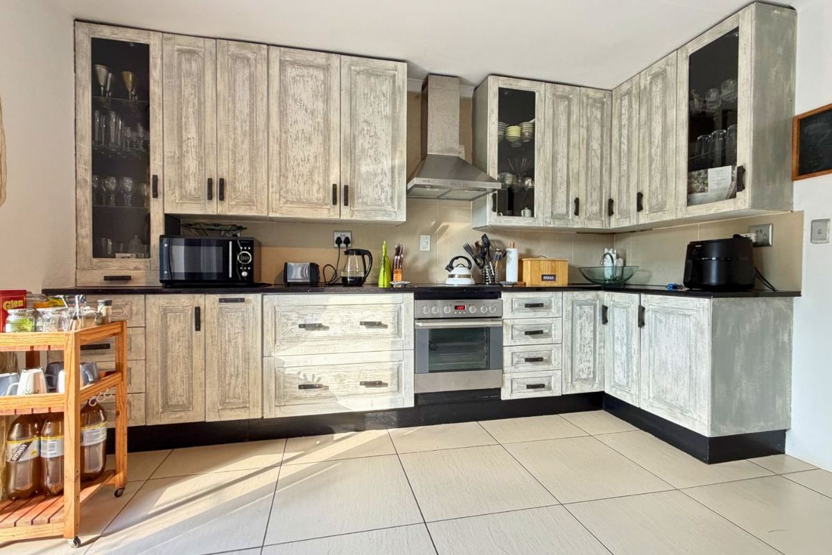 A functional kitchen featuring distressed-finish cabinetry, dark countertops, a built-in oven, stainless steel extractor fan, and tiled flooring.