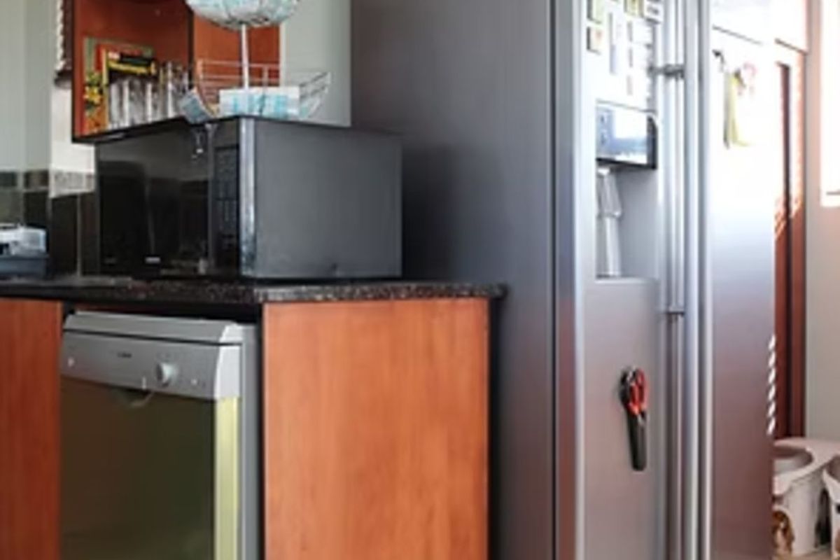 A functional kitchen area featuring wood-finish cabinetry, granite countertops, and space for a large refrigerator and dishwasher.