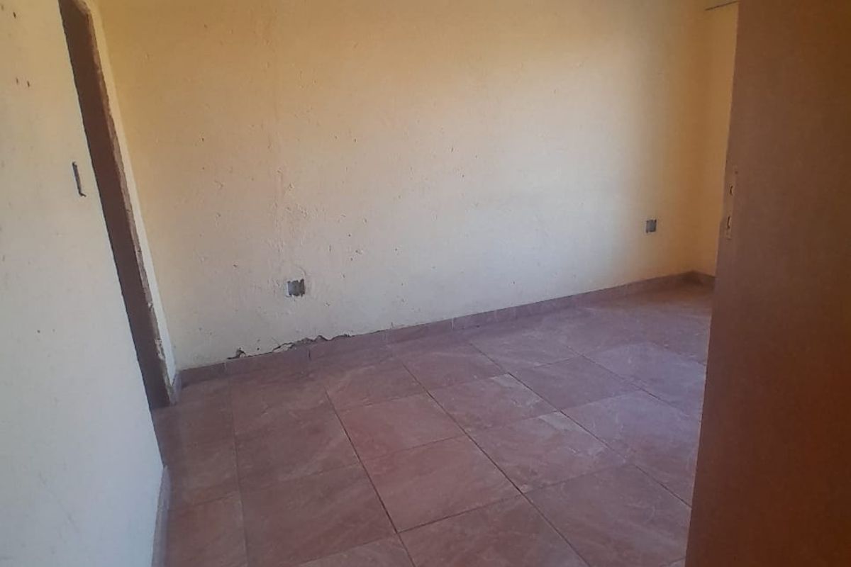 An empty bedroom featuring tiled flooring, a decorative ceiling with crown molding, and yellow-painted walls requiring maintenance.