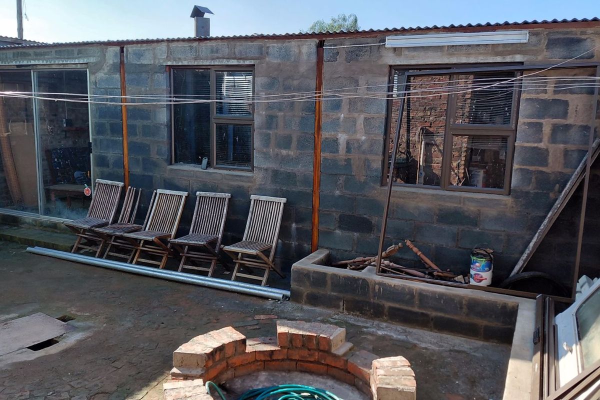 Rear exterior view of the property featuring unfinished concrete block walls, sliding glass doors, and a brick fire pit area in the yard.