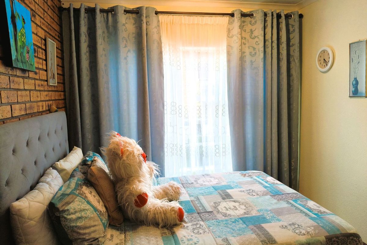 A bedroom featuring a textured face-brick feature wall and a window dressed with floor-to-ceiling curtains.
