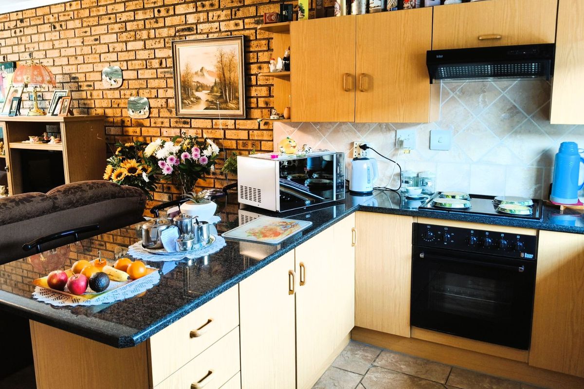 A functional kitchen featuring light wood cabinetry, dark granite countertops, a built-in oven, and a distinctive exposed brick feature wall.