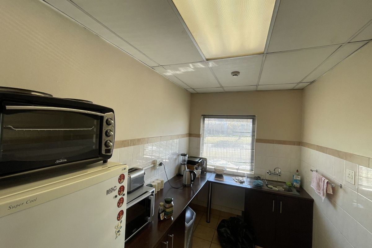 A functional industrial kitchenette featuring dark cabinetry, a stainless steel sink, tiled splashbacks, and a drop ceiling with integrated lighting.