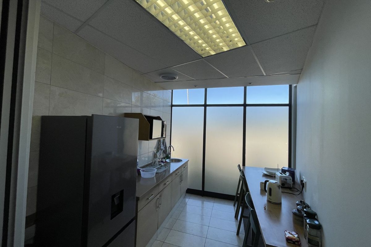A functional office kitchenette featuring tiled flooring, built-in cabinetry, a stainless steel sink, and a large window providing natural light.