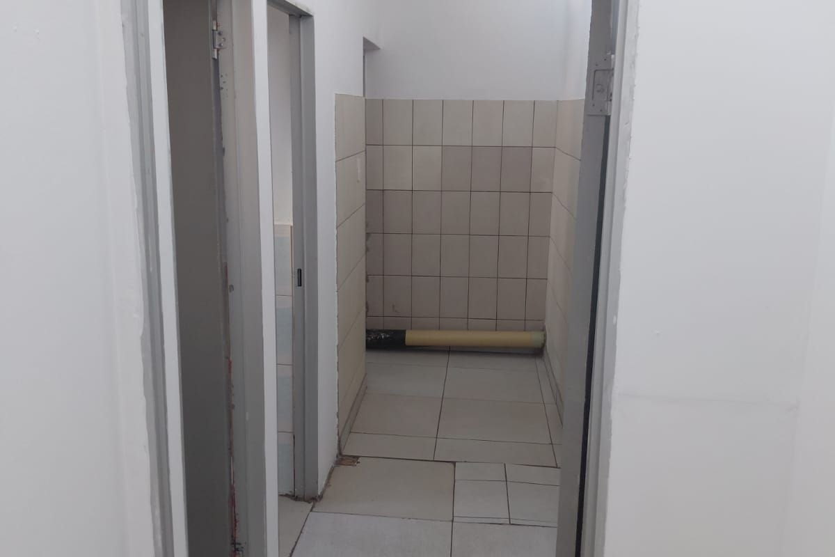 A functional office restroom facility featuring tiled flooring and walls, with multiple cubicle access points and clear signage.
