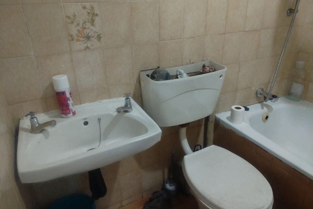 A dated bathroom featuring a wall-mounted basin, a toilet with a missing cistern lid, and a bathtub with integrated shower fixtures.