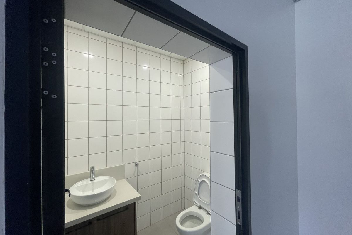 A clean, modern bathroom featuring white wall tiles, a vanity with a vessel sink, and a standard toilet.