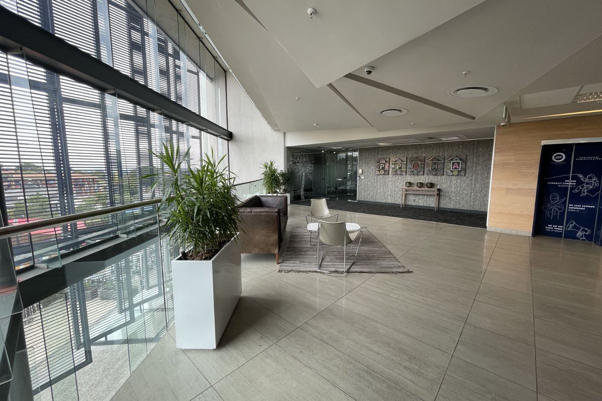 A modern, spacious reception or lounge area featuring large floor-to-ceiling windows, tiled flooring, and contemporary architectural ceiling details.