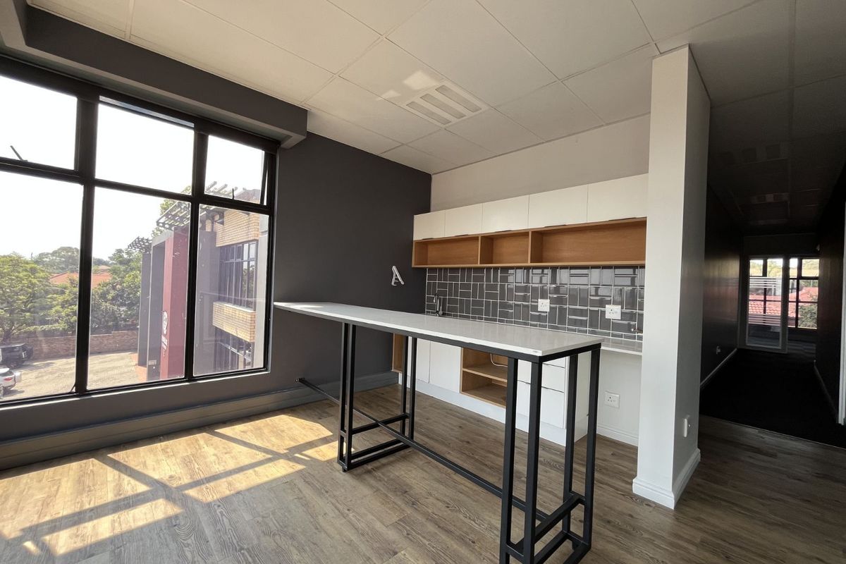 Modern office kitchenette featuring built-in cabinetry, subway tile backsplash, and a sleek breakfast bar, set against large windows with natural light.