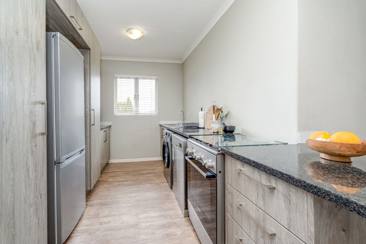 A functional kitchen featuring wood-look cabinetry, granite countertops, a built-in oven with hob, and space for laundry appliances.