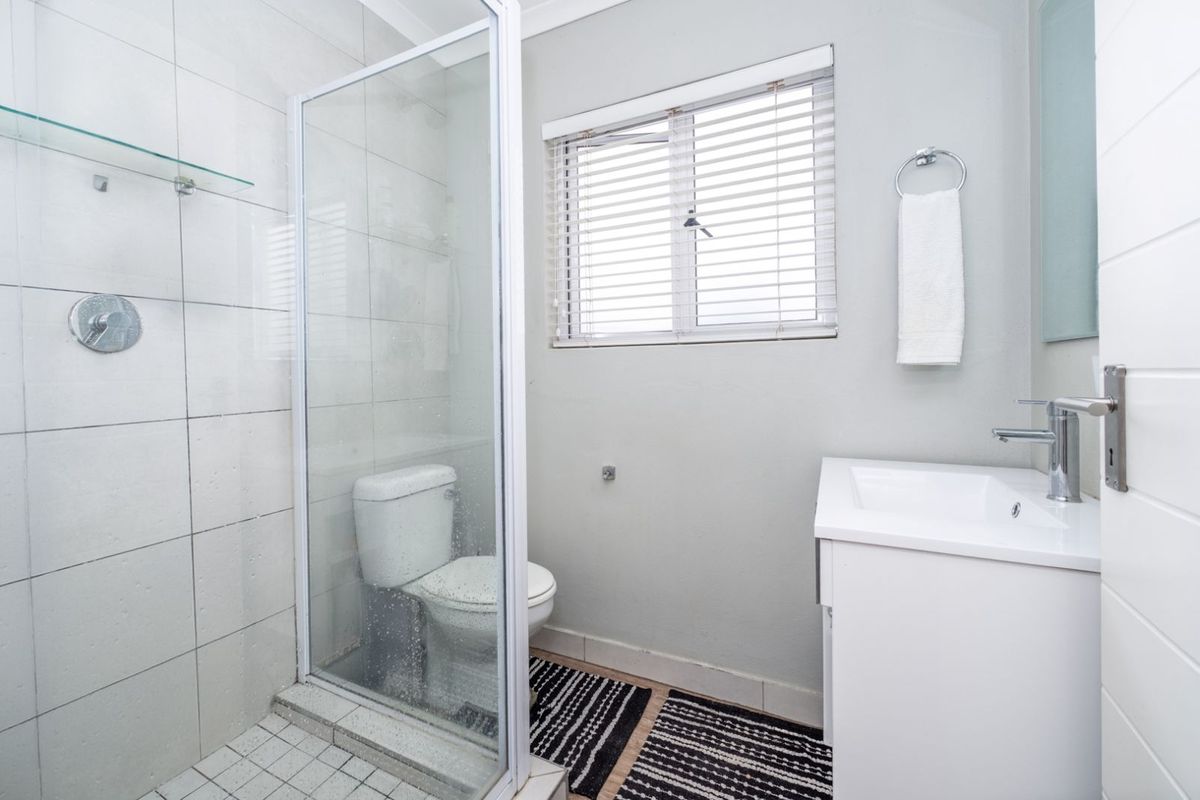 A clean, modern bathroom featuring a glass-enclosed shower, a white vanity with a basin, and a toilet, finished with neutral wall tiles.