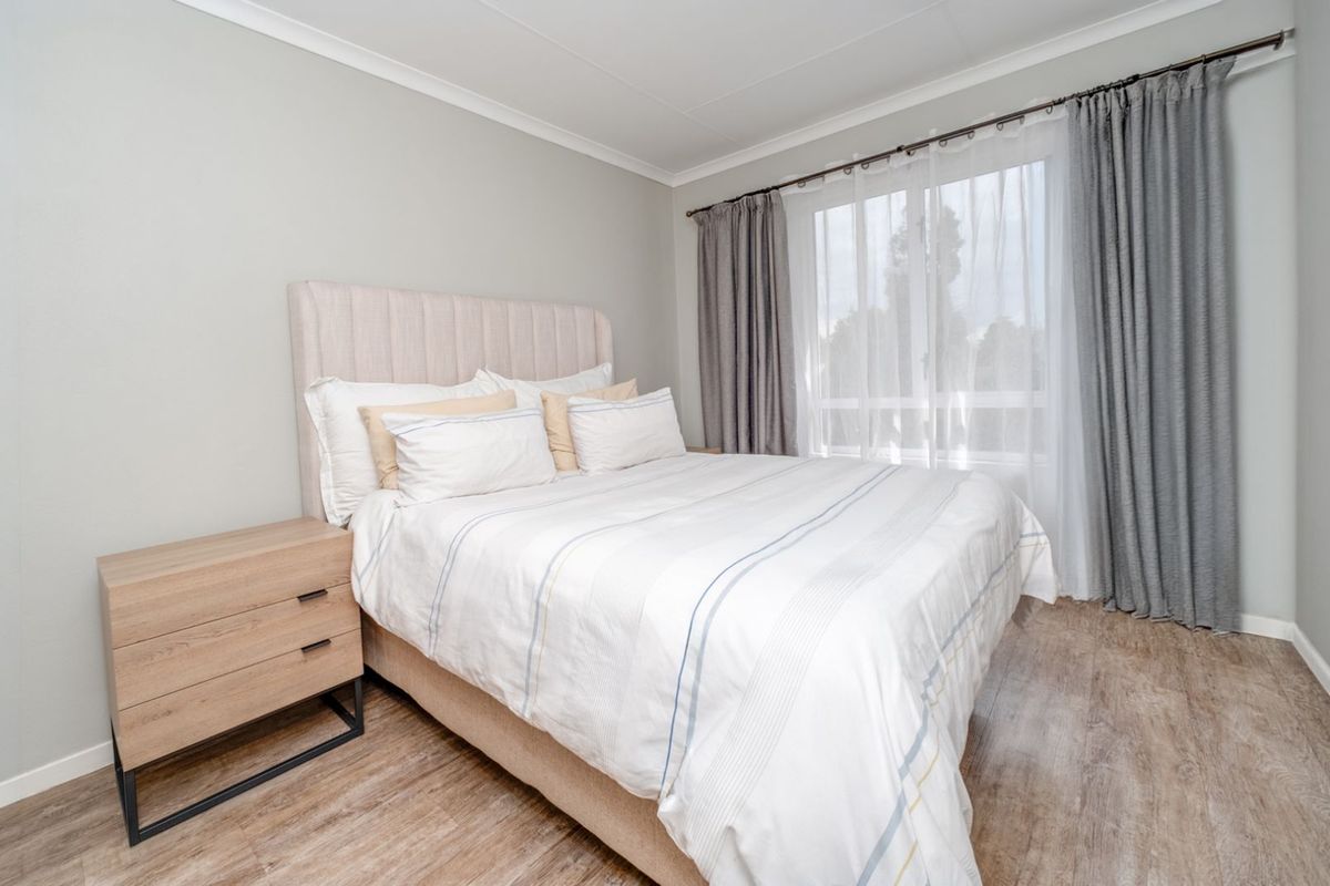 A well-maintained bedroom featuring light wood-look flooring, neutral wall tones, and a large window with integrated curtain tracks.