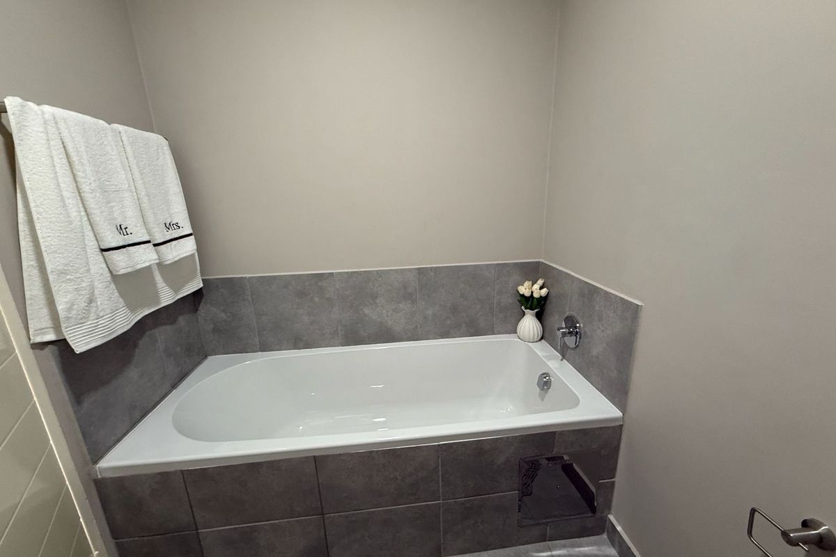 A clean bathroom featuring a built-in bathtub with grey tiled surround and chrome fixtures.