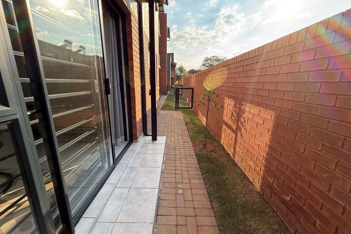 A side walkway featuring paved brick paths, a high brick boundary wall, and large sliding glass doors leading into the townhouse interior.